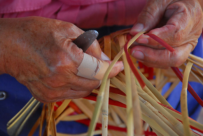 close up of hands weaving strips of cane to make a basket